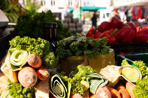 Auf dem Markt liegen frische Möhren, Lauch, Kräuter und rote Paprika neben weiteren Gemüsesorten.