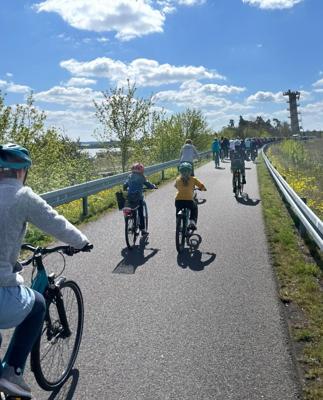 Mehrere Radfahrer fahren auf einem asphaltierten Dammweg mit Geländern, begleitet von sonnigem Wetter und weitem Himmel.