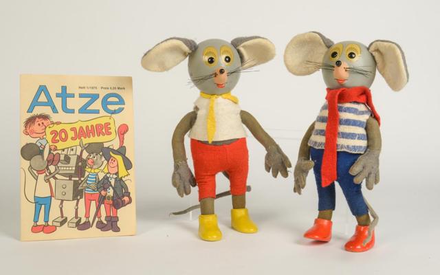 Neben dem Buchcover „Atze 20 Jahre“ stehen zwei Stoff-Mausfiguren mit bunten Kleidungsstücken vor hellem Hintergrund.