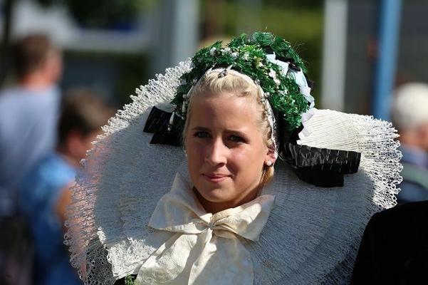 Eine blonde junge Frau trägt eine traditionelle Tracht mit großer weißer Spitzenhaube und grün-weißem Kopfschmuck.