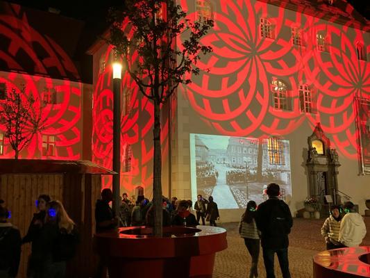 Im Schlosshof versammeln sich Besucher vor einer Fassade mit roten Lichtmustern und einer historischen Projektion.