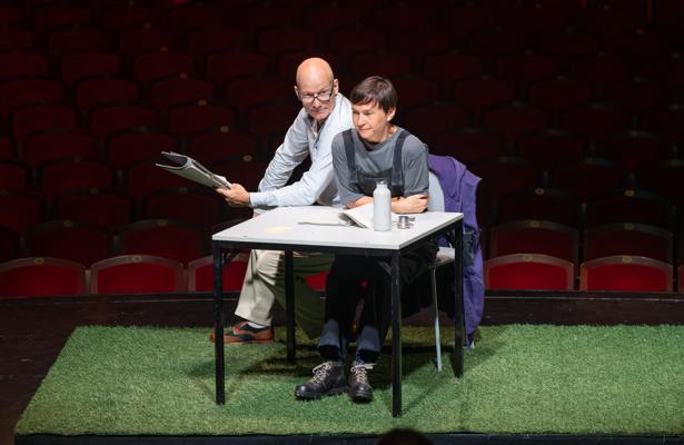 Auf der Bühne von Zwischen Welten sitzen zwei Darsteller an einem Tisch und lesen aus dem Roman von Juli Zeh und Simon Urban im Staatstheater Cottbus.