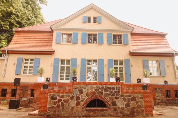 Das historische Herrenhaus des Ritterguts Kemmen hat eine helle Fassade, blaue Fensterläden und ein rotes Dach.