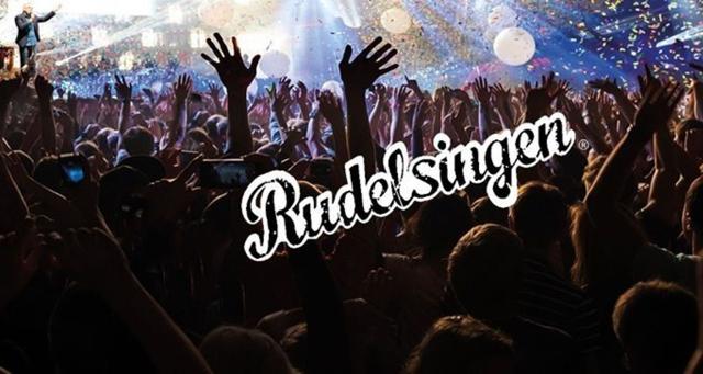 Viele Menschen recken bei Rudelsingen ihre Hände in die Luft, während das Wort „Rudelsingen“ über der Menge steht.