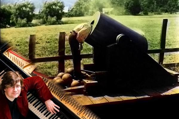Ein Pianist sitzt an einem Flügel im Freien, daneben lehnt eine Person über einer schwarzen Lokomotive auf einem Feld.