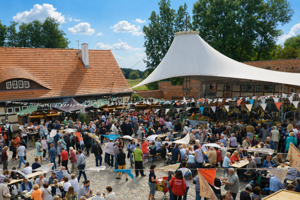 Im Burghof drängen sich viele Besucher zwischen Ständen, Festzelt und Wimpelketten unter einem sonnigen Himmel.