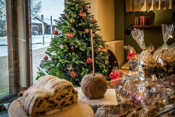 Ein geschmückter Weihnachtsbaum steht neben verpackten Geschenken und Gebäck, während draußen Schnee vor dem Fenster liegt.